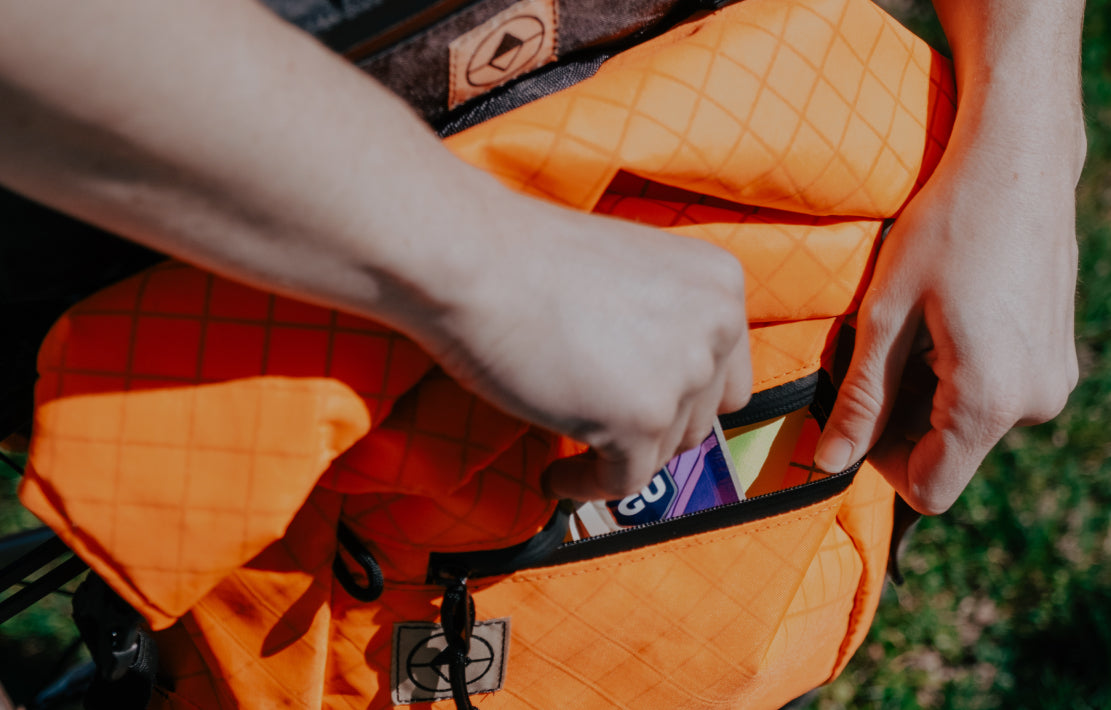 hands reaching into front pocket of a blaze orange bikepacking pannier