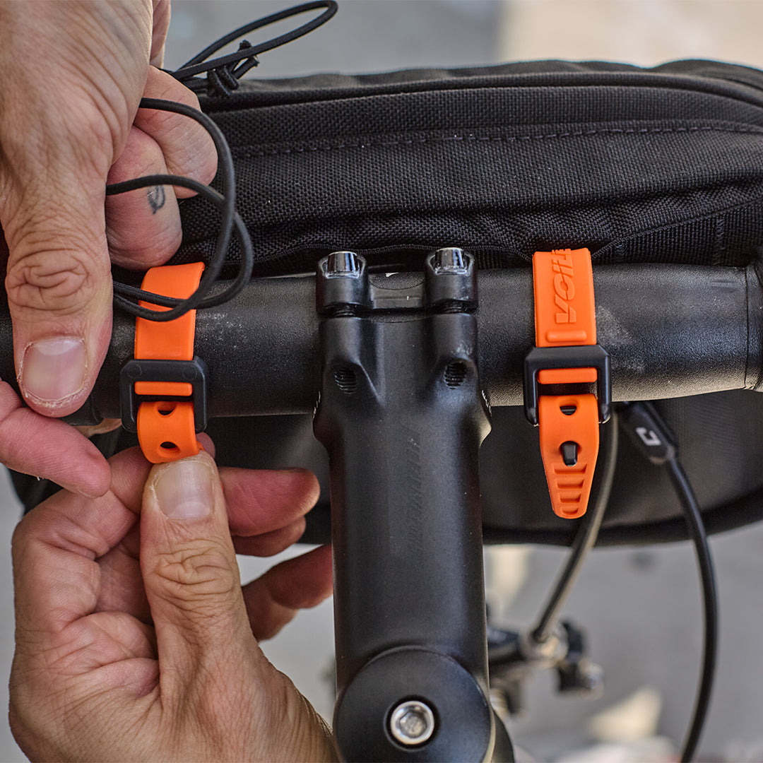 Person adjusting an orange strap on a black handlebr bag with a blurred background all-groups