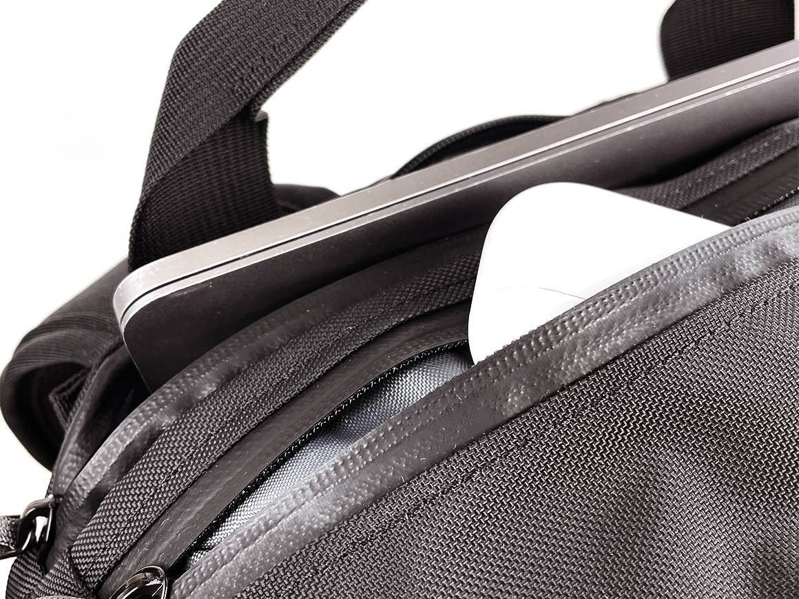 Close-up of a black travel backpack with a zippered compartment open, showing a silver laptop and a white item stored inside.