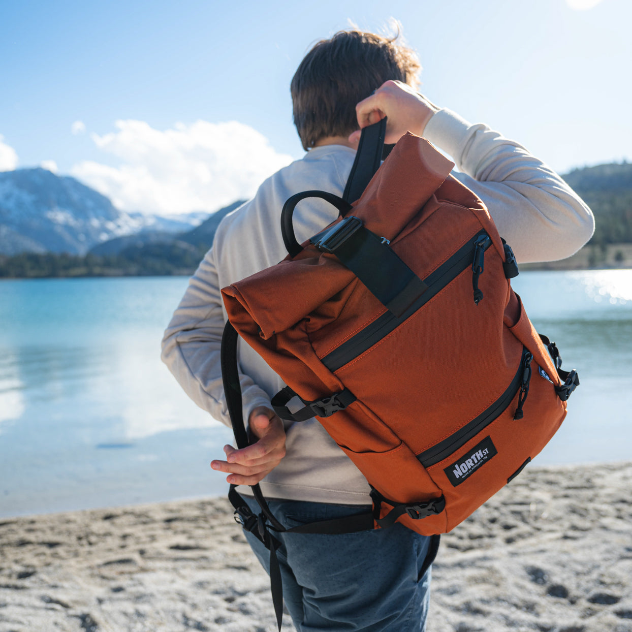 man putting on backpack on the beach