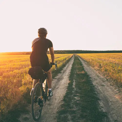 Man biking through a field on a gravel road.