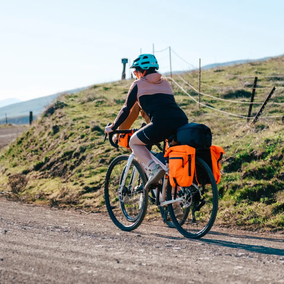 woman biking along a gravel road with bikepacking bags