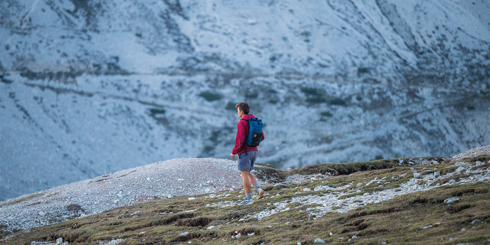 man hiking on a snowy mountainside with an ocean blue daypack