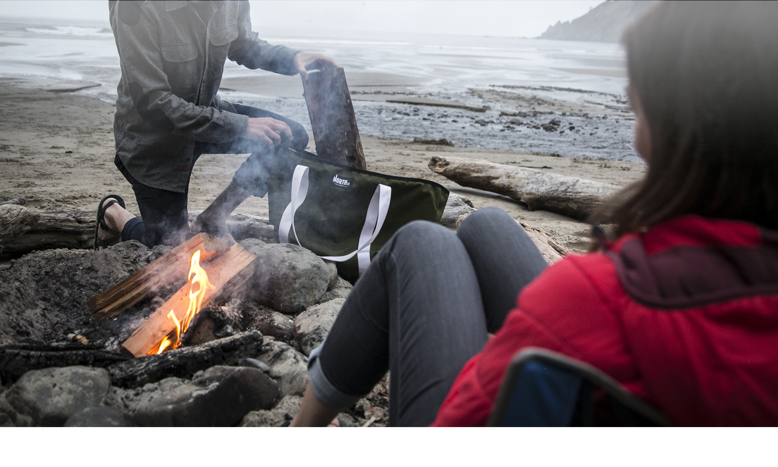 A couple builds a campfire on a beach with a Tote bag. | North St Bags