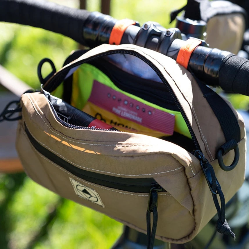Lifestyle shot of Handlebar Pack mounted to bicycle, zipper open with snacks and items inside.  - North St Bags all-groups