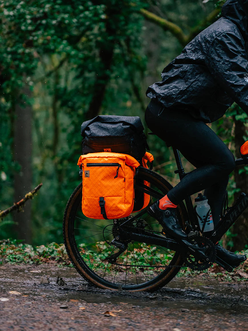 Cylist riding on a wet muddy pack with bikepacking panniers and trunk bag. | North St Bags - all-groups