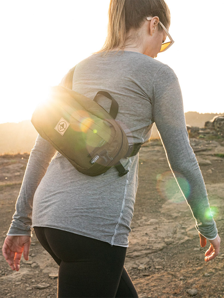 Woman walking along a trail at sunset wearing a Coyote Sling Pack- North St. Bags all-groups