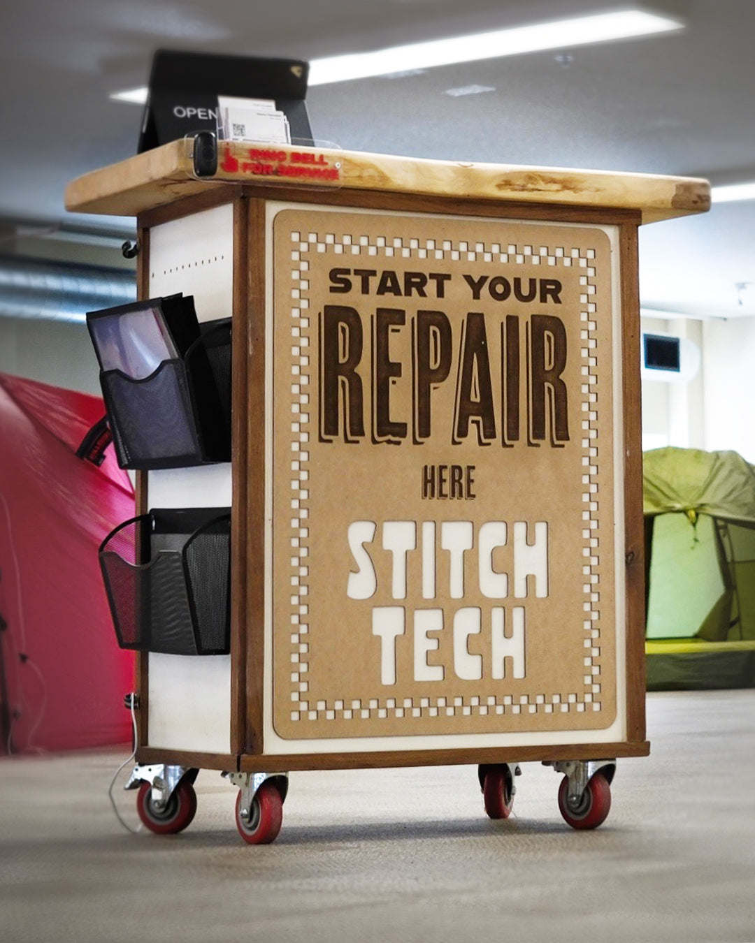 Kiosk with a sign reading 'Start Your Repair Here Stitch Tech' in an indoor setting.