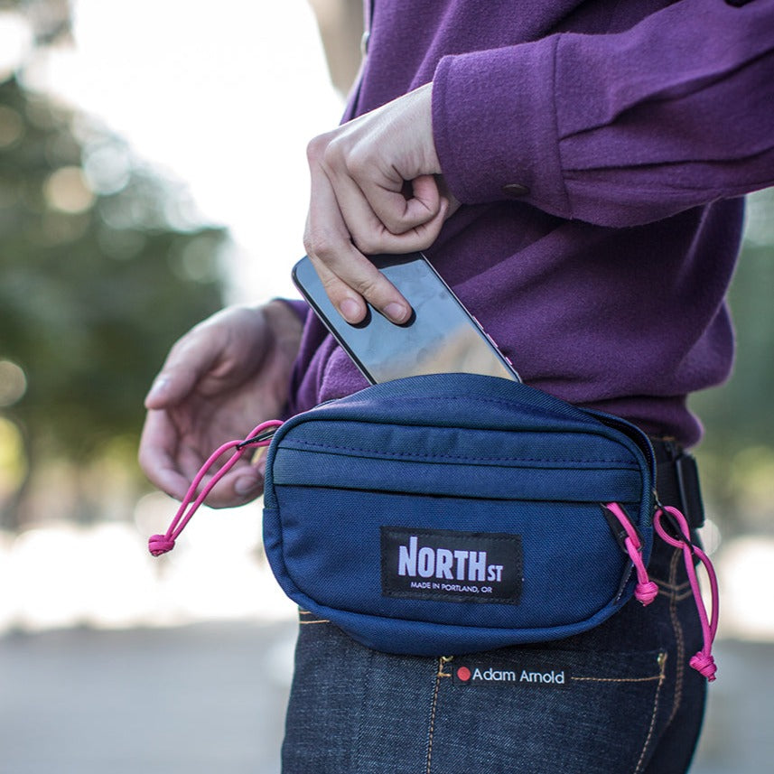 Guy putting phone into a blue Pioneer 8 Fanny Pack - North St Bags | all-groups