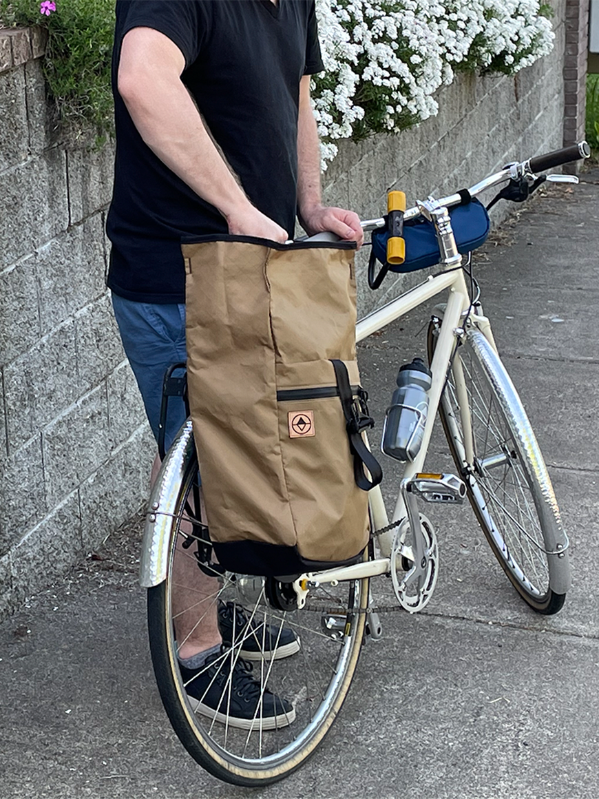 Cyclist packing a Commuter Macro Pannier on a bike. Showing roll-top open. - North St Bags all-groups