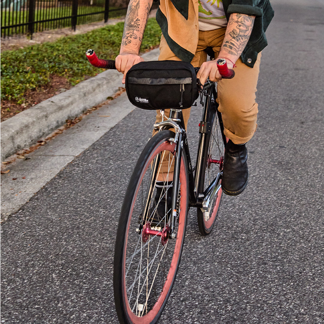 Person riding a bicycle on a road with a black bag attached to the handlebar. all-groups