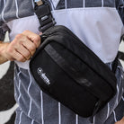 Person holding a black crossbody bag with a visible brand logo, wearing a striped shirt. all-groups