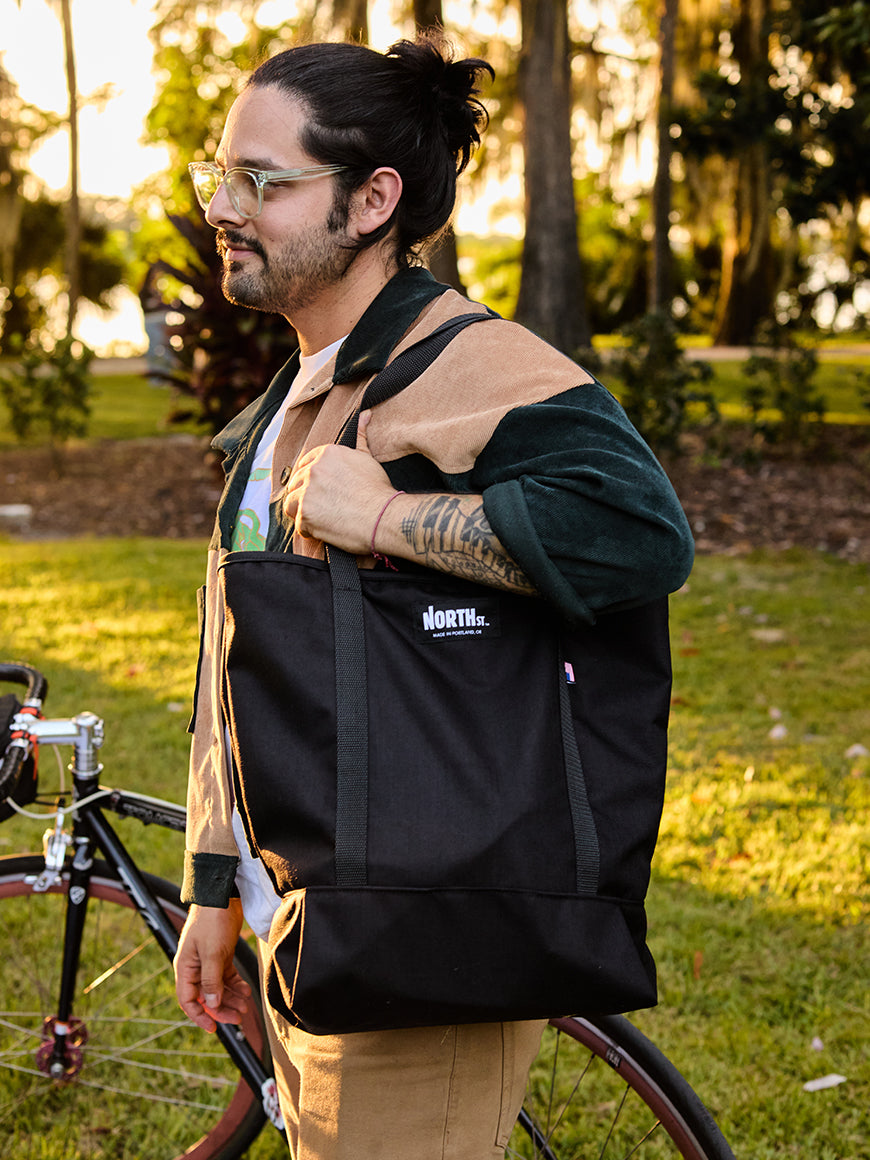 Man holding a black bag with 'The North Street' logo in a park setting