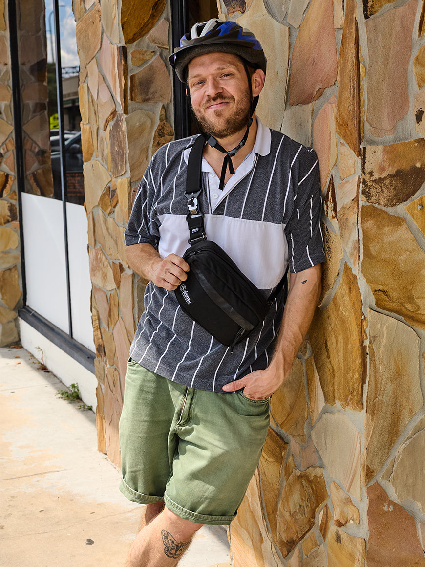 Man with a helmet and a sling bat standing against a stone wall.