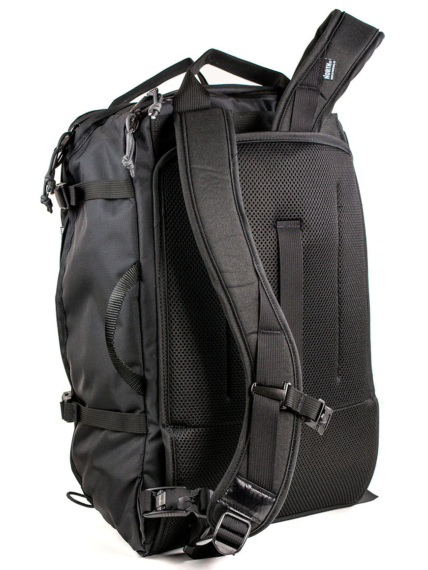 Back view of a black travel backpack showing stow-able backpack straps and carry handles on a white background. 