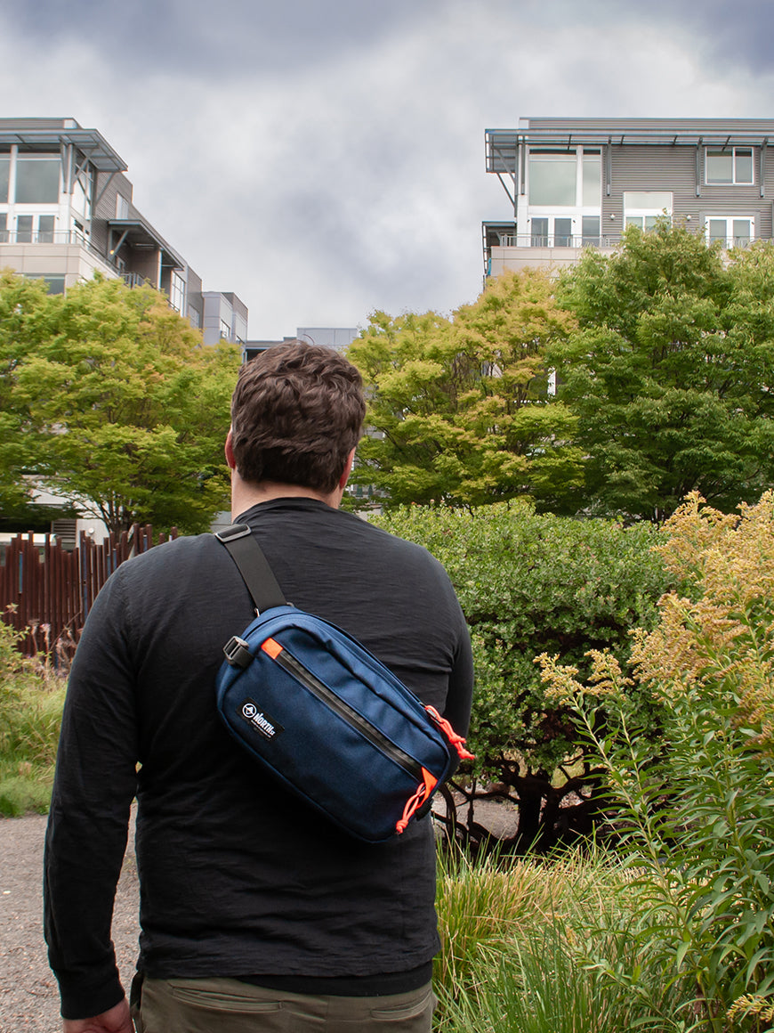 Man in city park wearing a blue and orange sling pack all-groups