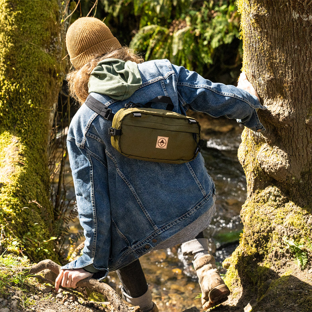 Guy climbing down a river bank on a trail wearing a Pioneer 12 as a Sling Pack - North St Bags - all-groups