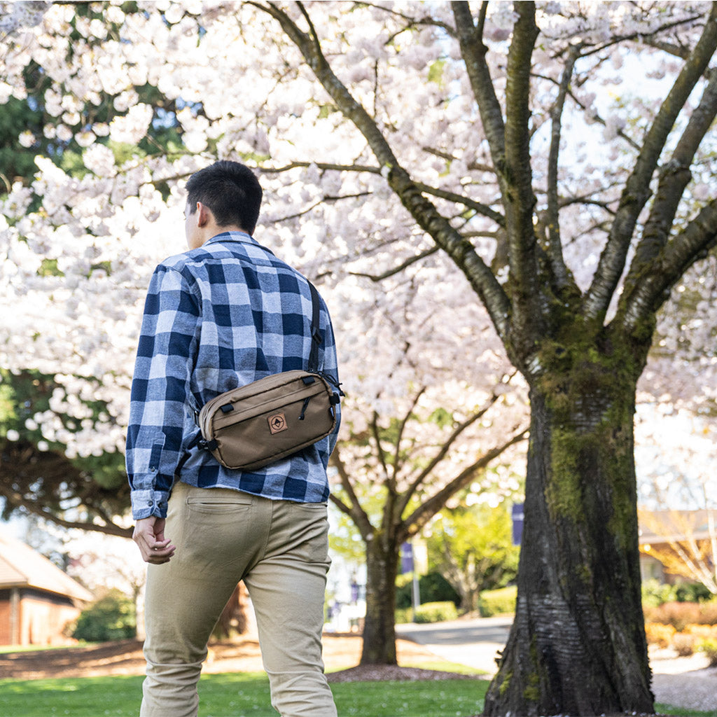 Guy walking under a cherry blossom tree wearing a Pioneer 12 as a Sling Pack - North St. Bags all-groups