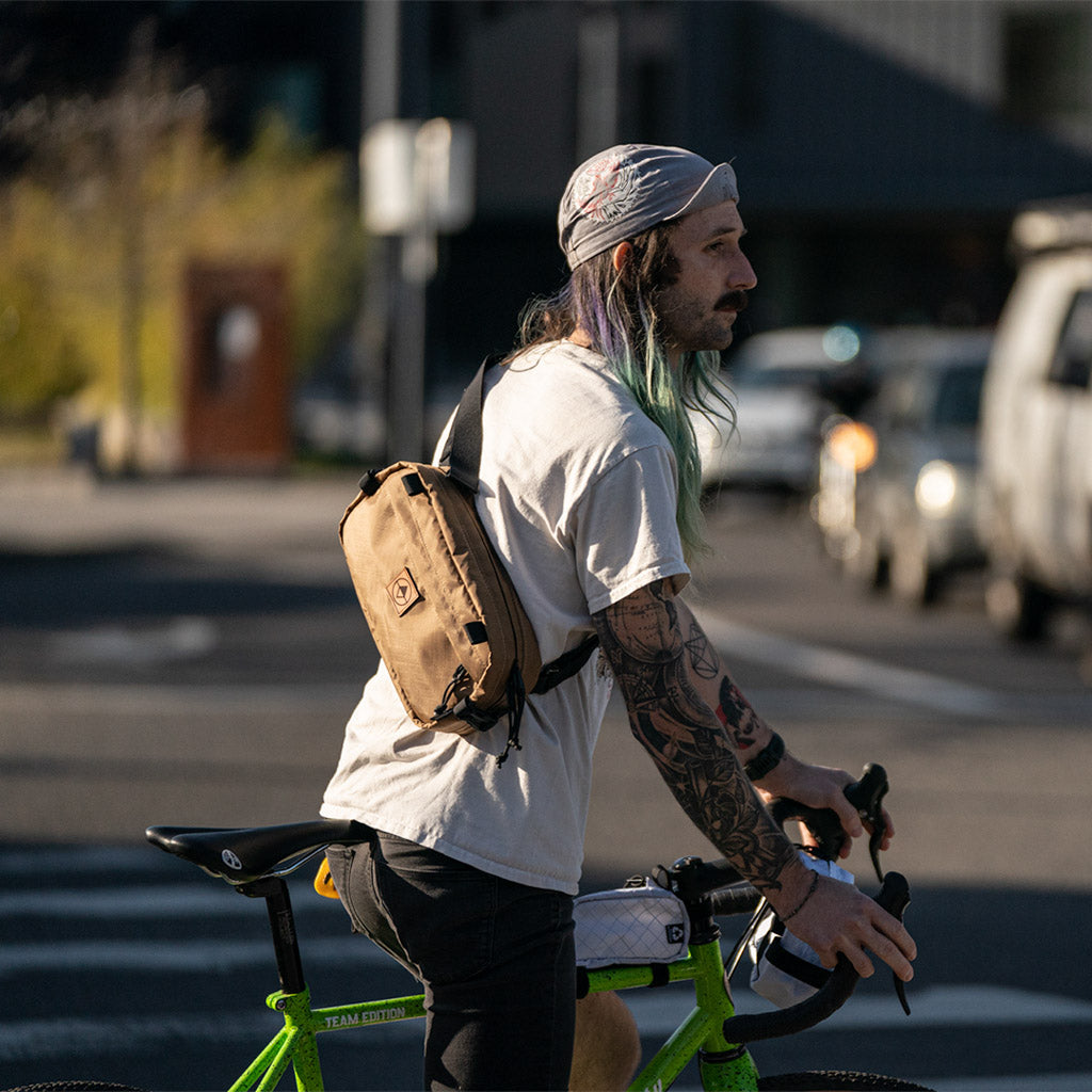 Guy on a bicycle wearing a cap and Coyote Pioneer 12 as a Sling Pack - North St. Bags all-groups
