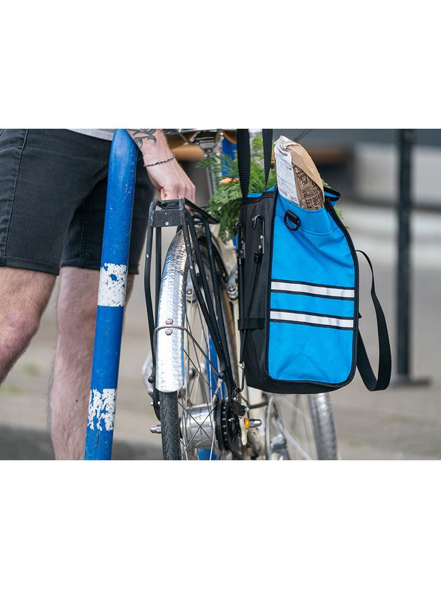 Cyclist mounting a bright blue pannier loaded with groceries to a bike. - North St. Bags all-groups